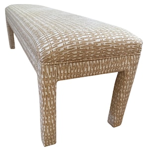 May include: A rectangular upholstered bench featuring a repeating tan and white geometric pattern across the seat and four sturdy legs. The fabric has a textured appearance with a consistent woven design covering the entire surface of the furniture.