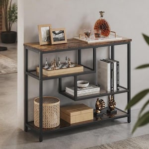 Könnte beinhalten: Ein Konsolentisch mit einer dunkel gemaserten Holzplatte und einem schwarzen Metallrahmen. Er verfügt über drei offene Regale mit einer Glaskaraffe auf einem Tablett, zwei Bilderrahmen, einem Holzschachspiel, Büchern, einem Korb und zwei goldenen Handskulpturen.
