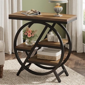 Peut inclure: Une table d'appoint avec un cadre circulaire en métal noir et trois étagères en bois. L'étagère supérieure porte un magazine ouvert et une lampe. L'étagère centrale présente un vase en verre avec des fleurs roses et deux boîtes blanches.