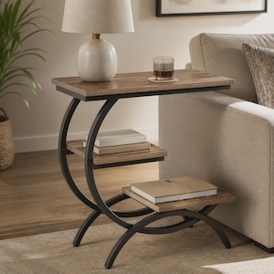Peut inclure: Une table d'appoint en forme de C avec une structure en métal foncé aux supports incurvés et trois étagères rectangulaires en bois. L'étagère supérieure porte une lampe blanche et un verre, tandis que les étagères inférieures accueillent des livres.