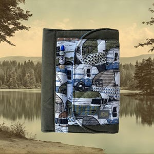 May include: A fabric notebook cover in olive green featuring a patterned front panel with vintage camper trailers in shades of blue, green, and white. The cover includes a pen loop with a decorative bead and a small tag with the text JEM.