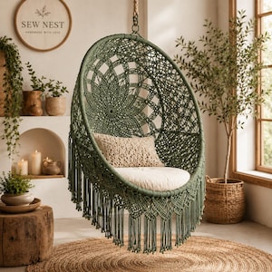 May include: A round, olive green macrame hanging chair featuring an intricate knotted pattern, long fringe detailing along the bottom, a beige rectangular throw pillow, and a circular off-white seat cushion suspended by a thick rope.