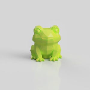 Op de afbeelding: Een limoengroen kikkerbeeldje met een geometrisch low-poly ontwerp met scherpe, hoekige facetten. Het kleine beeldhouwwerk is afgebeeld in een zittende positie en toont een gladde, matte oppervlaktestructuur en een uitgesproken uiterlijk.