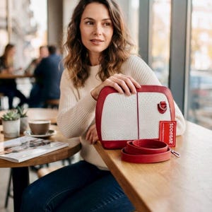 Peut inclure: Un sac à main structuré avec un panneau avant blanc texturé à motif peau de serpent, encadré par des bords en cuir rouge lisse. Le sac comprend une bandoulière en cuir rouge et une étiquette rectangulaire rouge avec le texte blanc SODAGAR.