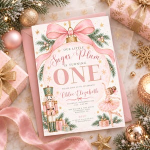 Op de afbeelding: Een rechthoekige verjaardagsuitnodiging met een grote roze kerstbal, een strik, een notenkraker en een ballerina. De tekst luidt: Our Little Sugar Plum is turning ONE, Chloe Elizabeth, Saturday, December 14th, 2:00-4:00 PM.