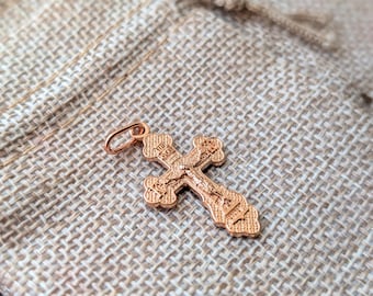 Könnte beinhalten: Ein rosegoldfarbener Metallkreuz-Anhänger mit detaillierter, geprägter religiöser Ikonografie und kyrillischen Schriftzeichen auf der Oberfläche. Das Kreuz hat eine texturierte Oberfläche und einen kleinen runden Ring zur Befestigung an einer Kette.