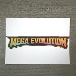 May include: A rectangular white sticker featuring the text MEGA EVOLUTION in a bold, stylised font. The letters transition from a vibrant green on the left to a warm orange and red on the right, enclosed within a dark, angular border.