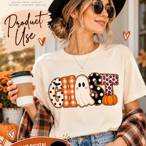 May include: A cream-colored t-shirt featuring the word GHOST in large, decorative letters. The G has black polka dots and a bat, the H has orange plaid, the O is a white ghost, the S has black polka dots, and the T has pink leopard print.