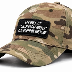 May include: A camouflage baseball cap featuring a rectangular black patch on the front. The patch displays the white text: MY IDEA OF "HELP FROM ABOVE" IS A SNIPER ON THE ROOF. The cap has a curved brim and a button on the top center.