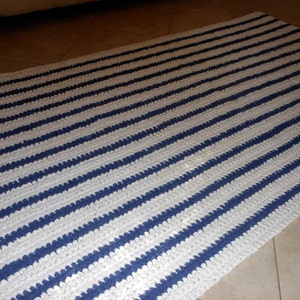 May include: A white and blue striped crocheted rug. The rug has a simple design with alternating stripes of white and blue.