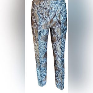 Puede incluir: Pantalones de largo completo con un patrón detallado de piel de serpiente en tonos marrón, negro y gris claro. Los pantalones tienen un corte de pierna recta con una costura central visible en la parte delantera de cada pierna, creando un aspecto estructurado.