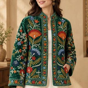 Puede incluir: Una chaqueta de terciopelo verde oscuro con cuello mao y mangas largas. La chaqueta está adornada con intrincados bordados florales multicolores en tonos rojo, naranja, azul y amarillo, con un patrón de borde vertical a lo largo del frente.