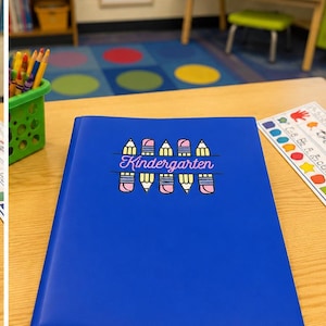 May include: A blue plastic folder featuring a graphic design of colorful pencils arranged above and below the word Kindergarten in pink script text. The folder is positioned on a wooden surface, showcasing a clean, professional school supply item.