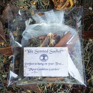 May include: A white tulle pouch filled with dried orange peels, cinnamon sticks, and other spices. The pouch has a label that reads "Yule Scented Sachet" and "Perfect to hang on your Tree... Moon Goddess Garden".