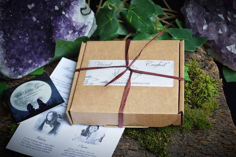 May include: A brown cardboard box with a red ribbon tied around it. The box has a label that says "Hand Crafted" and "Moon Goddess Garden.com".