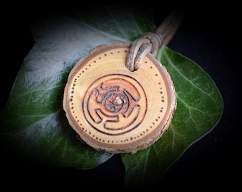May include: A wooden pendant with a carved spiral design, hanging from a brown leather cord. The pendant is on a green leaf.