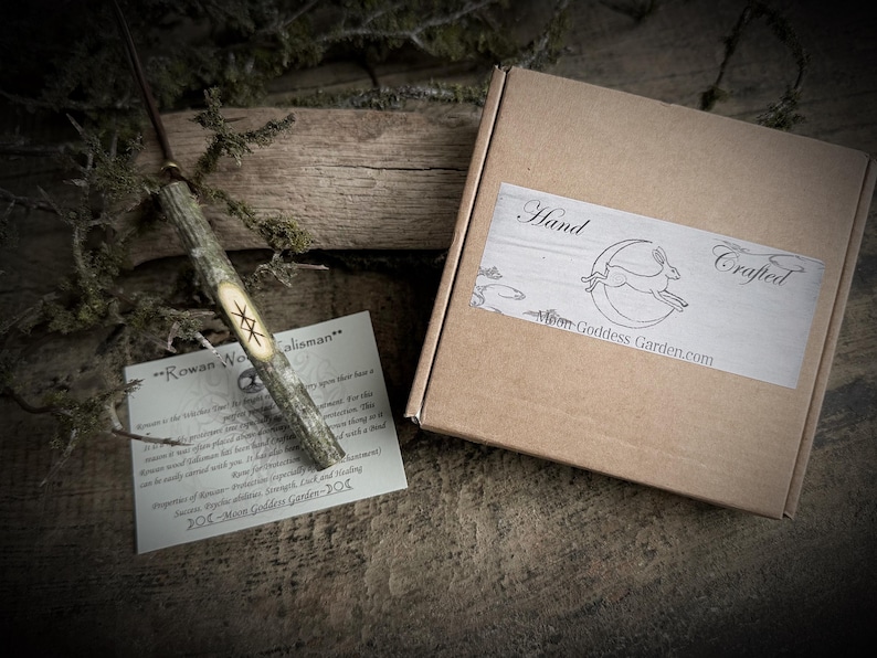 May include: A handcrafted wooden wand with a carved star design, accompanied by a card and a cardboard box with a label that reads "Hand Crafted" and "Moon Goddess Garden.com". The wand is made of natural wood.