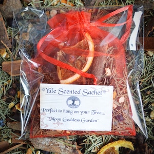 May include: A red mesh bag filled with dried orange slices, cinnamon sticks, and other spices. The bag is labeled "Yule Scented Sachet" and "Perfect to hang on your tree... Moon Goddess Garden".