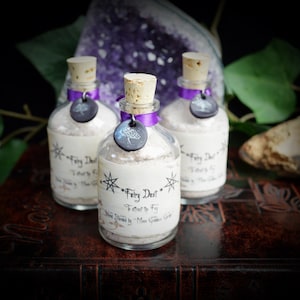 May include: Three small glass bottles with cork stoppers and purple ribbon accents. Each bottle contains a white powder and has a label that reads "Fairy Dust - To attract the Fay" and "Hand Blended by Moon Garden Grimoire".