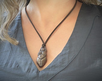 May include: A brown leather necklace with a brown ceramic pendant shaped like a female figure.