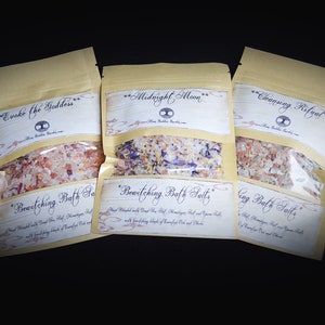 May include: Three small brown paper bags filled with bath salts. The bags are labeled "Evoke the Goddess", "Bewitching Bath Salts", "Midnight Moon", "Bewitching Bath Salts", "Cleansing Ritual", and "Cleansing Bath Salts".