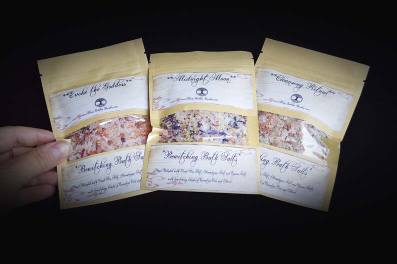 May include: Three small brown paper bags filled with bath salts. The bags are labeled "Evoke the Goddess", "Bewitching Bath Salts", "Midnight Moon", "Bewitching Bath Salts", "Cleansing Ritual", and "Cleansing Bath Salts".