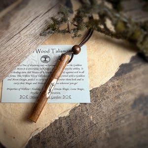 K&ouml;nnte beinhalten: Ein h&ouml;lzernes Talisman mit einer Lederschnur und einer Holzperle. Das Talisman ist mit einem Symbol graviert und liegt auf einem Papier mit Text &uuml;ber seine Eigenschaften. Der Hintergrund ist eine rustikale Holzoberfl&auml;che.