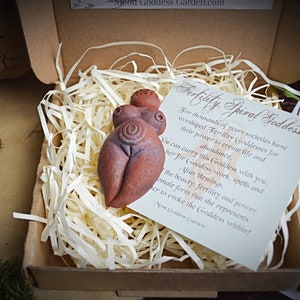 May include: A terracotta figurine of a fertility goddess with a spiral design on her belly. The figurine is in a small cardboard box with shredded paper. The box also contains a card with the text "Fertility Spiral Goddess" and a description of the goddess.