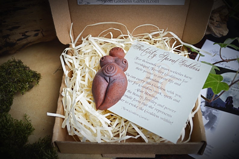 May include: A terracotta figurine of a fertility goddess with a spiral design on her belly. The figurine is in a small cardboard box with shredded paper. The box also contains a card with the text "Fertility Spiral Goddess" and a description of the goddess.