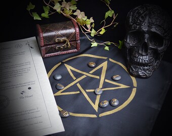May include: A black cloth with a gold pentagram design and black stones placed on the points of the star. A black skull and a small wooden chest are also on the cloth.