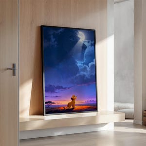 May include: A framed vertical wall art print featuring a small lion cub standing on a dark orange landscape under a deep blue sky. A large, ghostly lion face appears in the clouds above, illuminated by a bright white moon in the upper centre.