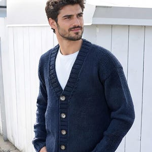 Op de afbeelding: Een marineblauw gebreid vest met een V-hals, een geribbelde knoopsluiting met vier zichtbare knopen en lange mouwen met geribbelde boorden. Het kledingstuk wordt gedragen over een effen wit T-shirt en een blauwe spijkerbroek.