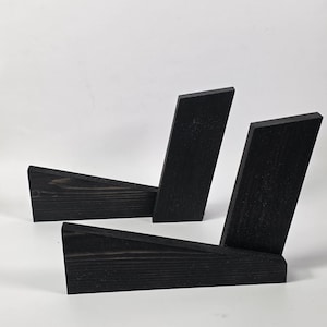 May include: Two black wooden display stands, each featuring a horizontal base and an angled upright support. The wood grain is visible through the dark finish, and the structures are designed to hold items at an incline for clear visibility.