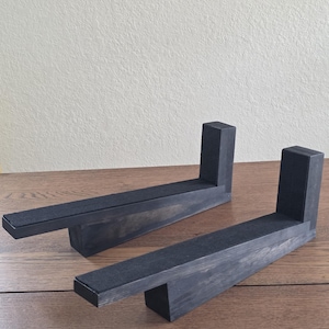 Op de afbeelding: Twee L-vormige houten standaards met een donkergrijze beitsafwerking. Elke standaard heeft een lange horizontale basis met een verticale steun aan één uiteinde en een strook zwart vilt op het bovenoppervlak van het horizontale gedeelte.