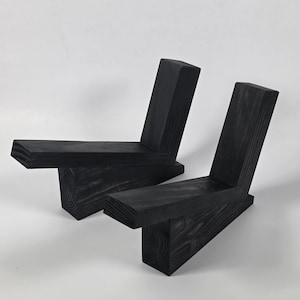 May include: Two black wooden objects, each constructed from three joined rectangular blocks of wood. The pieces feature a visible wood grain texture and are arranged in an angular, L-shaped configuration with a protruding base and upright back.