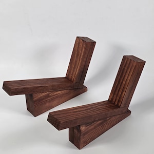 Può includere: Due fermalibri in legno tinto marrone scuro, ciascuno costruito con tre blocchi rettangolari uniti ad angoli per formare un profilo a Z, con una trama visibile delle venature del legno e bordi netti su tutta la struttura.
