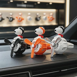May include: Three Snoopy car air fresheners shaped like vintage airplane engines. Each features a white Snoopy figure wearing a pilot cap and red scarf, mounted on a round body with a spinning propeller. Colors are black, orange, and white, all marked #01.