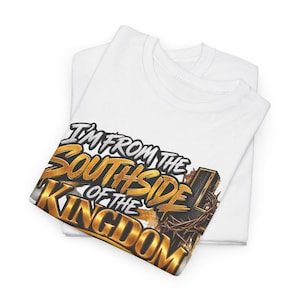 以下が含まれることがあります： 「I'M FROM THE SOUTHSIDE OF THE KINGDOM」という文字がメタリックゴールドと黒の太字でデザインされた白いTシャツ。プリントの右側には茨の冠のイラストが描かれています。