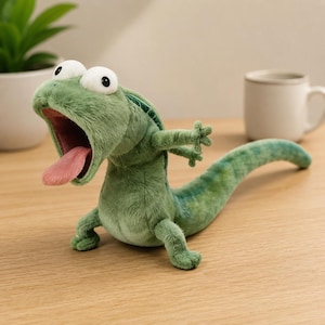 May include: A plush green lizard toy with a wide-open mouth, a protruding pink tongue, and large white eyes with black pupils. The stuffed animal features a textured fabric body, short arms, and a long, curved tail extending to the right side.