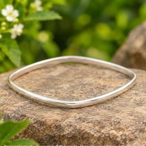 May include: A polished silver-toned bangle bracelet with a square-shaped silhouette. The bracelet features a smooth, continuous metal band with rounded corners and a reflective surface, showcasing a simple and clean design.