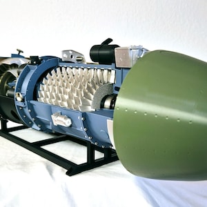 May include: A detailed scale model of a jet engine featuring a prominent olive green intake cowl, a blue-grey casing, and exposed silver-colored turbine blades. The mechanical assembly is mounted on a black metal stand, showcasing internal components.
