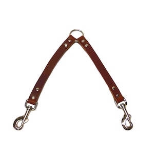 May include: Brown leather dog leash with two metal clips and a metal ring in the center.
