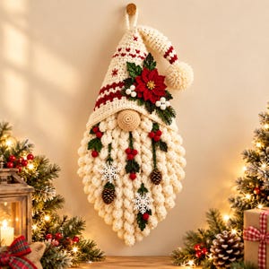 May include: A cream-colored crocheted gnome wall hanging featuring a tall pointed hat with red accents, a large round nose, and a textured beard adorned with red berries, green leaves, white snowflakes, and small brown pinecones.