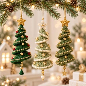 Peut inclure: Trois décorations de sapin de Noël en crochet suspendues verticalement. L'arbre de gauche est vert foncé avec des perles rouges et des étoiles dorées. L'arbre central est vert sauge avec des bordures blanches et des flocons dorés.