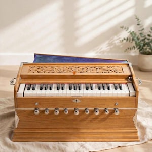 May include: A wooden harmonium musical instrument featuring a keyboard with white and black keys, a row of silver knobs, and a carved floral panel on the top. The instrument includes a blue bellows section visible at the back of the wooden frame.