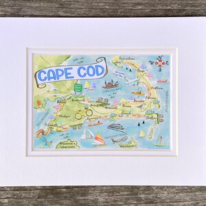 May include: A colorful illustrated map of Cape Cod, Massachusetts, with a blue banner that reads "CAPE COD". The map shows the towns and landmarks of the Cape, including Falmouth, Sandwich, Chatham, and Provincetown. The map is surrounded by a white border.