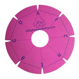 May include: A pink circular braiding disc with a central hole and cut-out notches. The disc has letters and lines printed on it, with the text "SallyBeadJewelry.com" and a cartoon image of a woman.