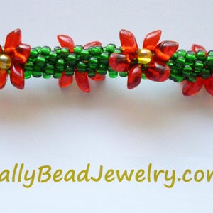 May include: A beaded jewelry piece featuring a green base with red flower accents and gold centers. The text "SallyBeadJewelry.com" is visible at the bottom. The piece is likely a bracelet or necklace.