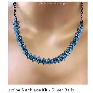 May include: A beaded necklace with a blue and silver color scheme. The necklace is made of small, round beads and has a dark chain. The text "Jewelry Designer" is at the top. The necklace is labeled "Lupine Necklace Kit - Silver Balls".