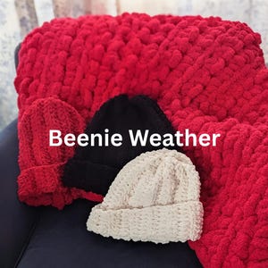 Puede incluir: Tres gorros de punto grueso en rojo, negro y crema, sobre una gran manta roja texturizada. El texto "Beenie Weather" está centrado en letras blancas sobre los gorros. Cada gorro presenta un borde acanalado y una textura de hilo grueso.